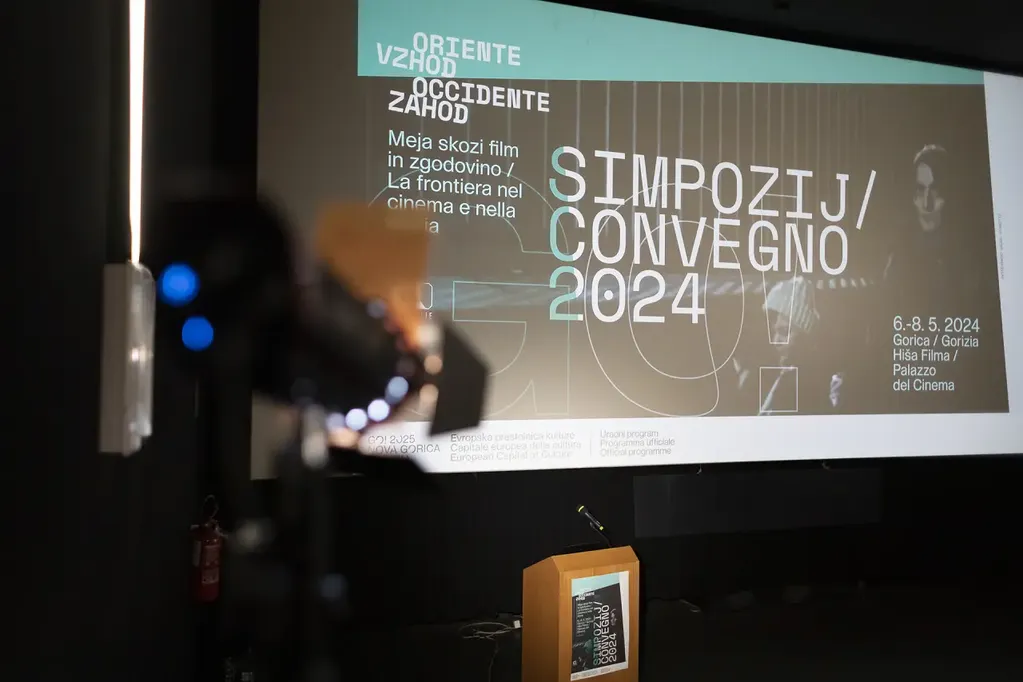 Photo of the lectern. In the background is a poster with the title: \&quot;Symposium / Convegno 2024\&quot;.